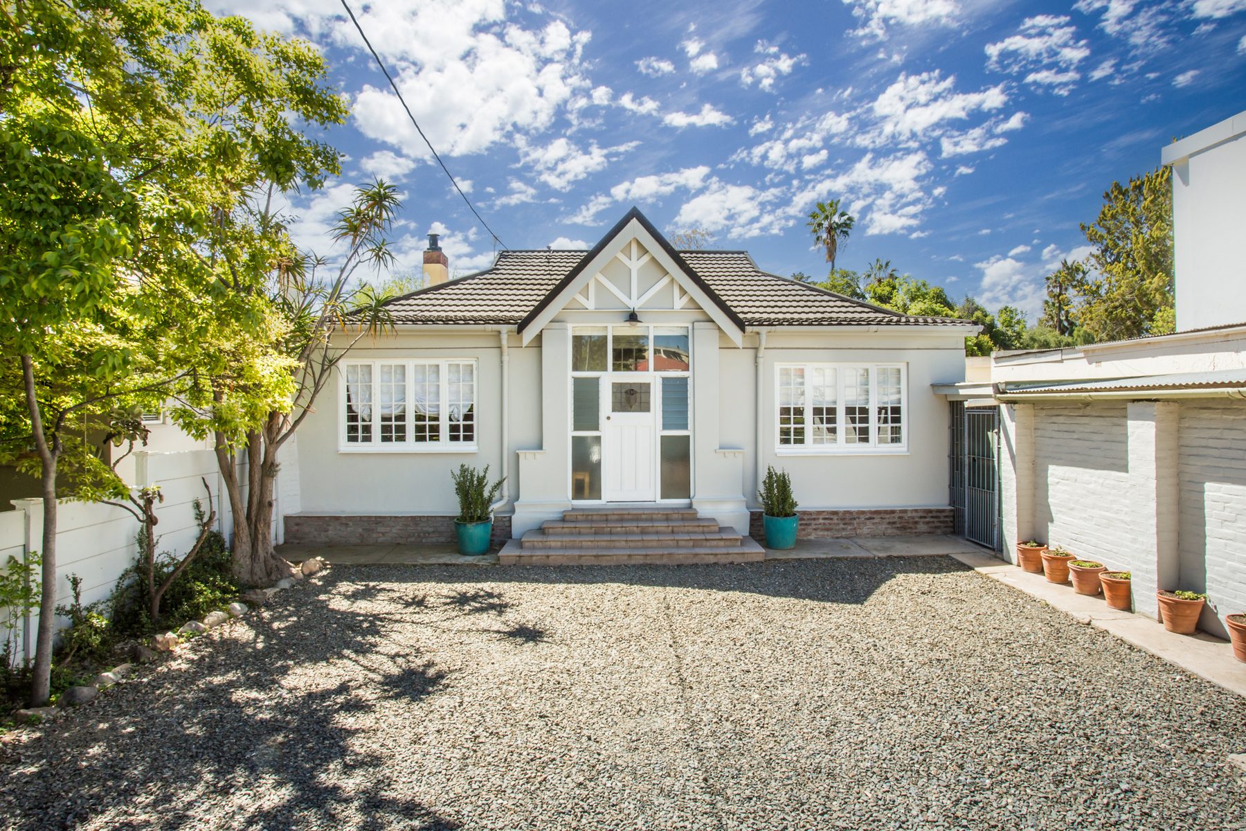 The front of Mirari, a white gabled house behind a gravel parking area