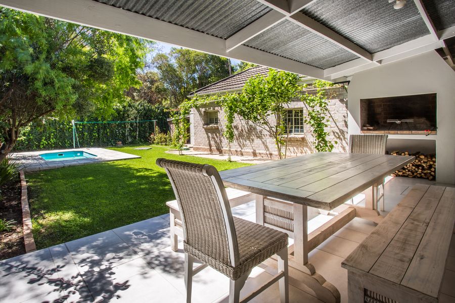 Covered patio with built-in braai and dining table, pool beyond